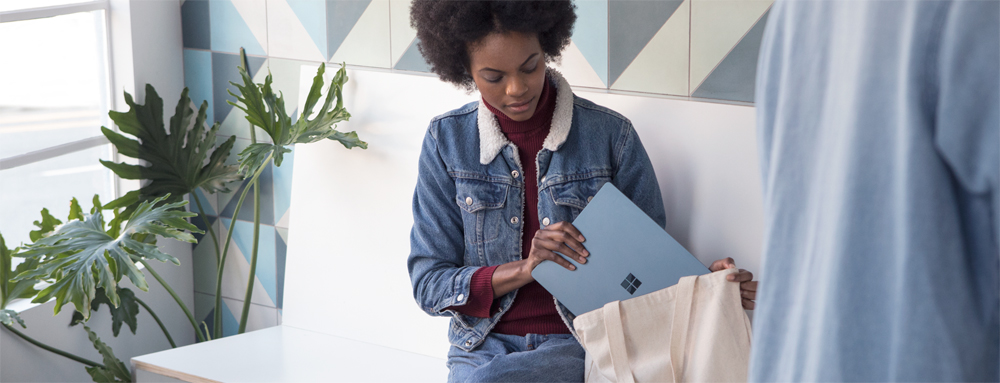 A woman wearing denim putting her Cobalt Blue Microsoft Surface laptop in her bookbag